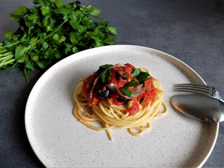 Un plat de spaghetti avec une sauce tomate aux anchois, aux câpres, aux olives et à l'ail